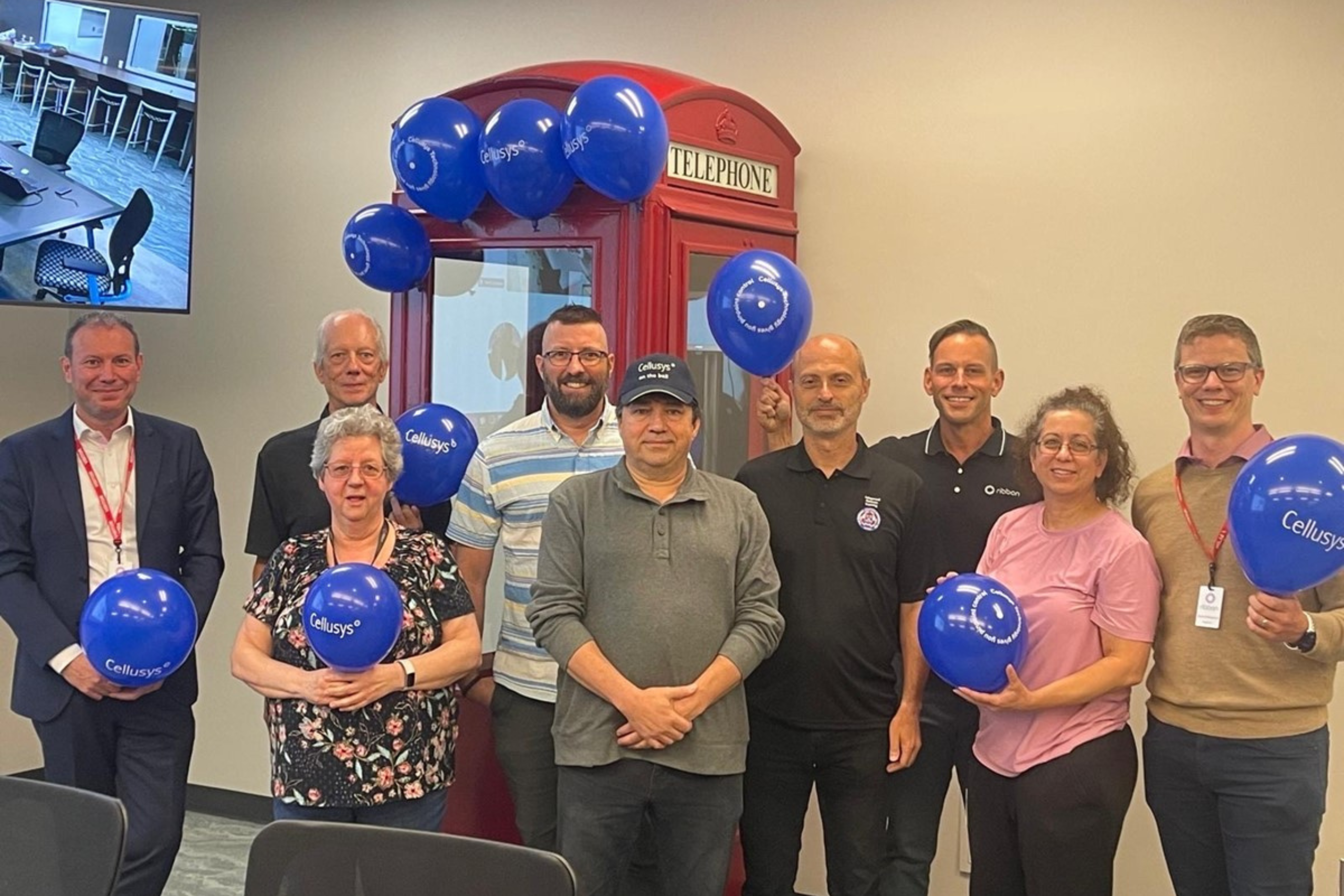 Staff of tech company Cellusys stand posing for a team photo holding blue balloons branded with the company logo.