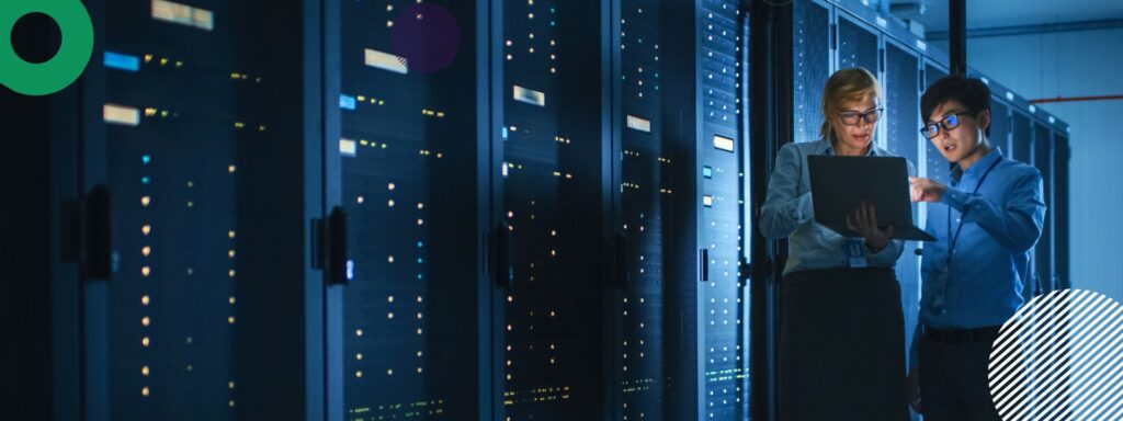 A featured image for a blog. The image shows two people standing and examining a laptop in a dark server room.