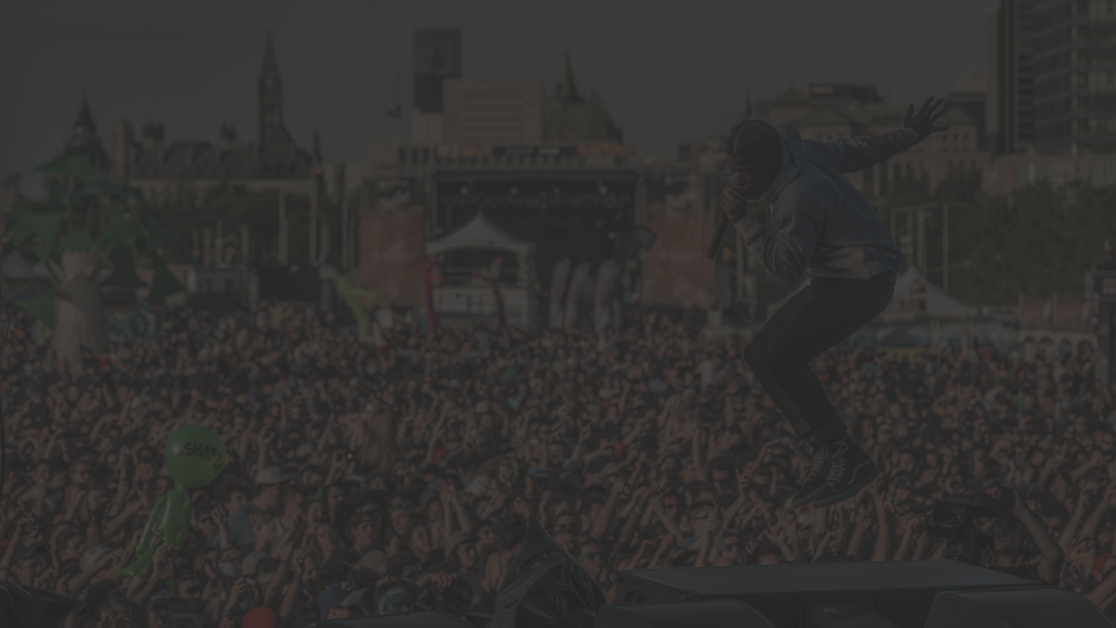 Performer jumping on stage during a large outdoor music festival, with a crowd in front of Ottawa’s skyline.
